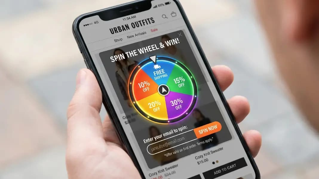A smartphone screen showing a spin to win popup wheel over an online store product page, with five colored prize segments visible and an email input field below the wheel ready for the participant to enter their address before spinning